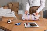 Seller packing shirt at table in office, closeup. Online store