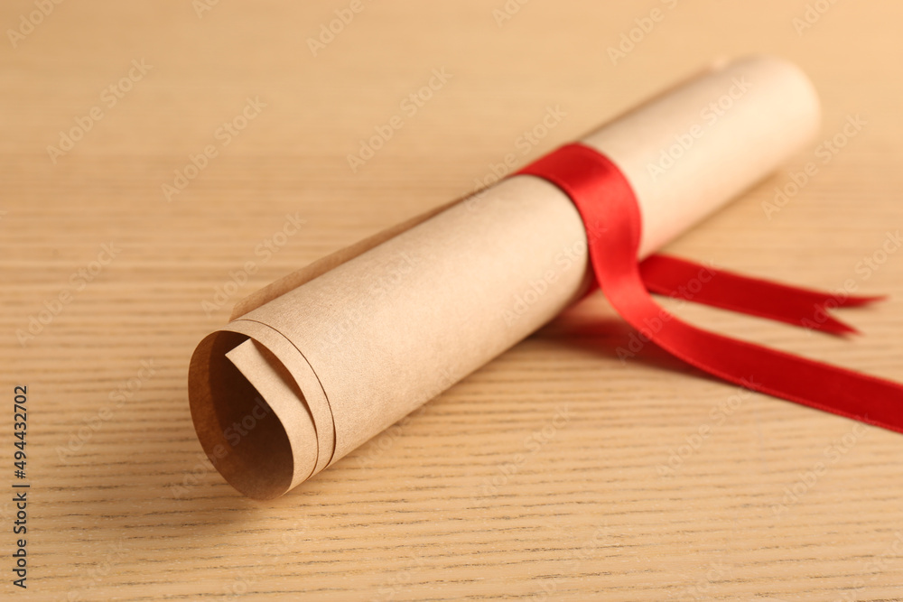 Graduation diploma tied with red ribbon on wooden table, closeup