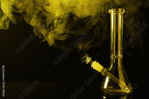 Glass bong and smoke on black background, space for text. Smoking device photo