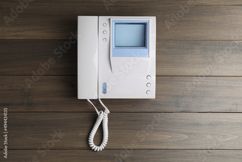Modern intercom system with handset on wooden background, top view