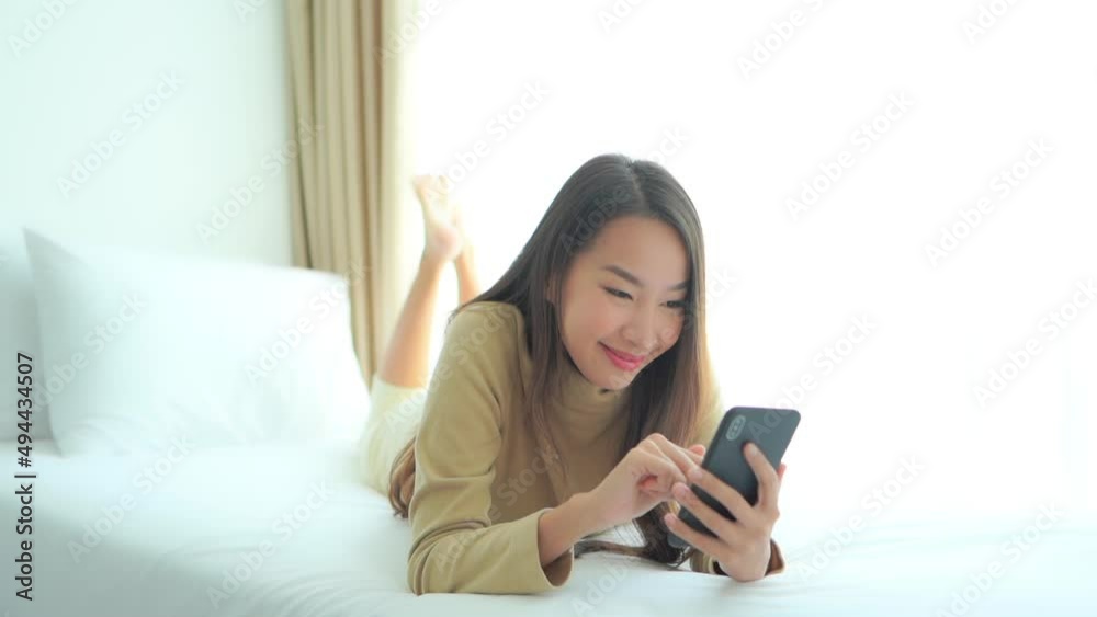 While lying on a large comfortable hotel bed, a young woman inputs data and swipes her smartphone screen. While lying on a large comfortable hotel bed, a young woman inputs data and swipes her smartphone screen.