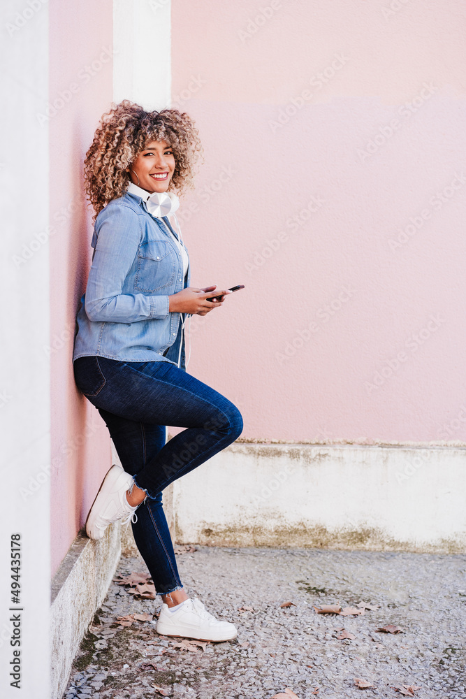 © Eva - happy curvy hispanic woman with afro hair in city using mobile phone and headset. Body positivity