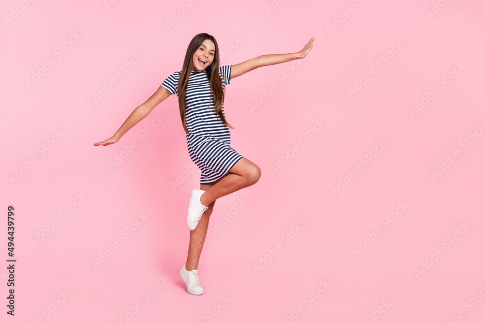 Photo of pretty cute girl dressed striped dress arms sides dancing empty space isolated pink color background