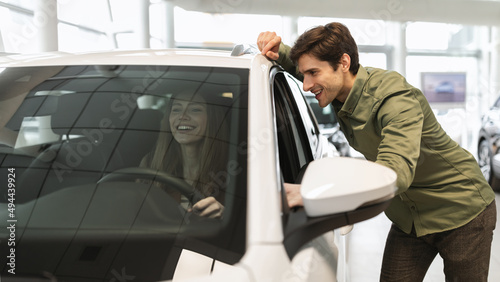 Joyful young Caucasian couple checking new luxury car before purchase at dealership automobile salon, banner design