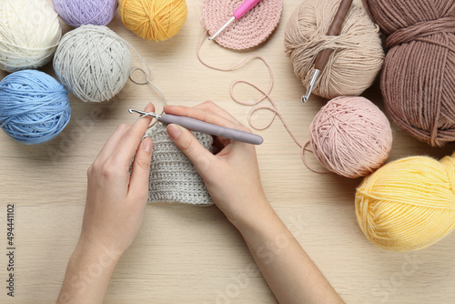 Woman crocheting with grey thread at wooden table, top view