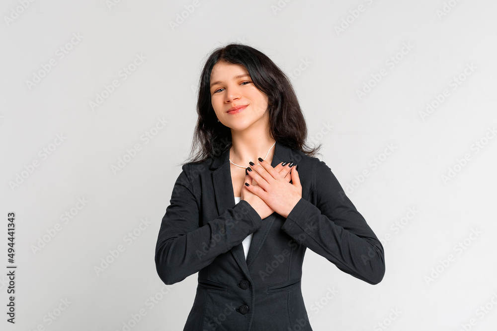 Portrait of beautiful brunette teen girl in black blazer, standing hopeful, anticipating, wishing to have something, daydreaming, standing over grey background Portrait of beautiful brunette teen girl in black blazer, standing hopeful, anticipating, wishing to have something, daydreaming, standing over grey background