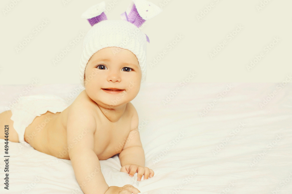 Portrait of happy smiling baby in knitted hat lying on the bed on white background Portrait of happy smiling baby in knitted hat lying on the bed on white background