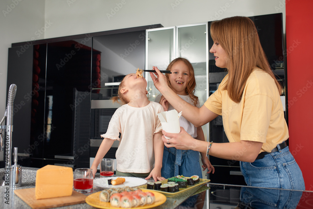 mom with two cute daughters, happy caucasian family having fun and eating sushi and rolls in the kitchen at home.