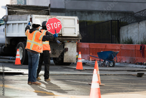 Construction workers with reflective vests and helmets holding a stop sign to organize traffic. Risk prevention work.