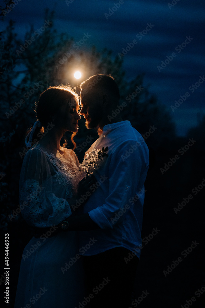 Romantic couple on a flowering meadow in the evening under the moonlight. Date.