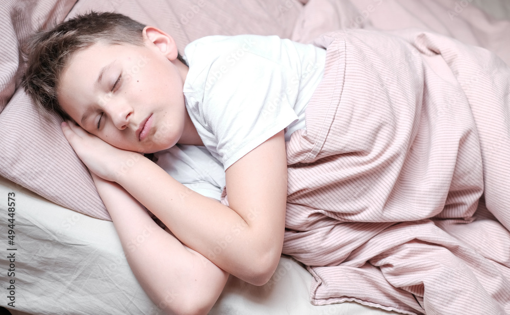 Boy teen sleeping on the bed in morning. Beds blanket is in light pink colors Boy teen sleeping on the bed in morning. Beds blanket is in light pink colors