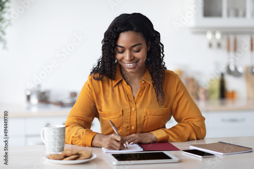 Positive black lady freelancer working from home, taking notes