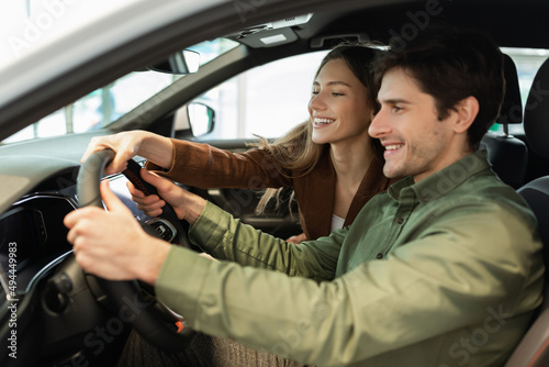 Happy young couple test driving new car at modern auto dealership