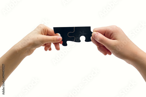 Two hands connected a black puzzle on a white background. Two black puzzles and two hands connect a puzzle on a white background close-up. Friendship or problem solving concept