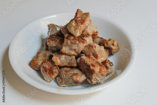 Cooked diced beef, on a white small plate, isolated on white background
