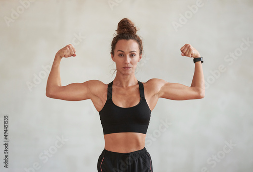 Portrait of modern young adult Caucasian woman wearing black sports outfit demonstrating her biceps on camera