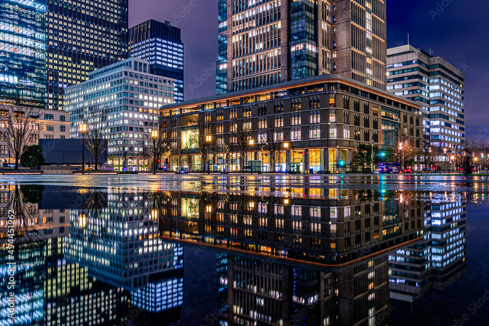 CHIYODA, TOKYO, JAPAN - MARCH 22, 2022 : Night city view of business buildings around the Marunouchi side of Tokyo Station after rain. Reflection photo with beautiful specular reflection.