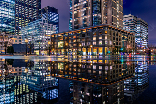 CHIYODA, TOKYO, JAPAN - MARCH 22, 2022 : Night city view of business buildings around the Marunouchi side of Tokyo Station after rain. Reflection photo with beautiful specular reflection.