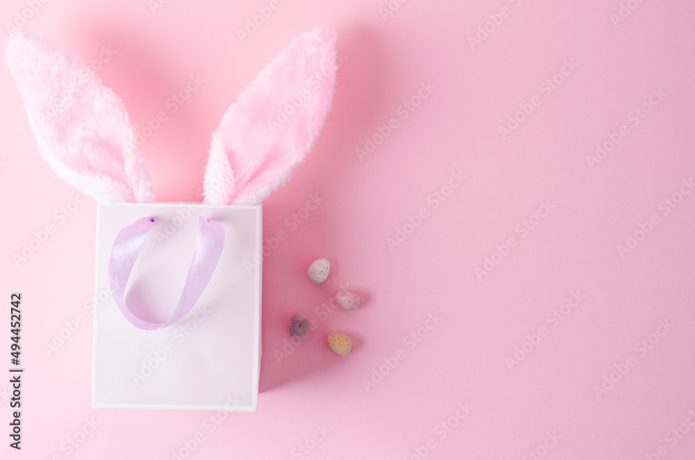 The concept of shopping for Easter. Paper bag on a pink background with bunny ears on a pink background, flat layout The concept of shopping for Easter. Paper bag on a pink background with bunny ears on a pink background, flat layout