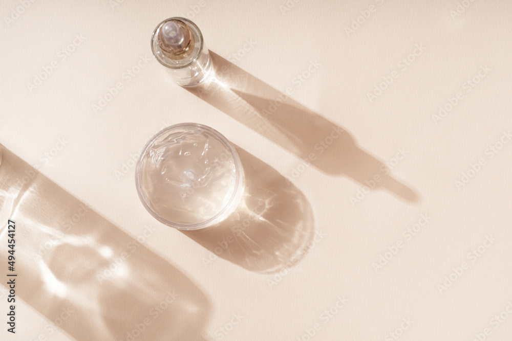 Cosmetics and liquid gel mask for care on a beige background. Shadows and glowing reflections from bottles. Cosmetics and liquid gel mask for care on a beige background. Shadows and glowing reflections from bottles.