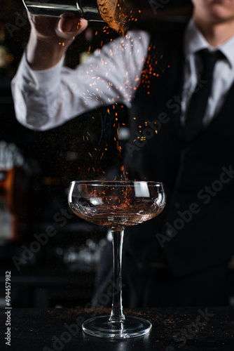 Close-up barman pours a ready made cold cocktail into glass on the bar counter.