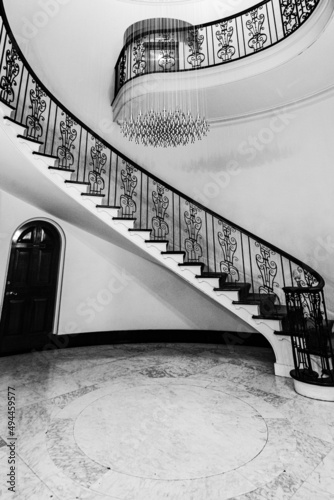 Vertical black and white shot of a staircase with a matching chandelier and a door on the wall photo