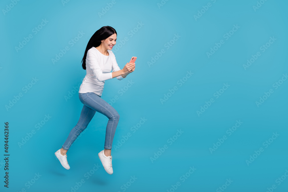 Full length body size view of attractive cheerful active girl jumping using device blog isolated on bright blue color background
