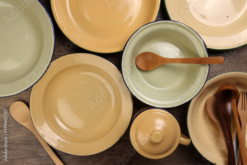 Varity of wooden metal spoon on enamel tin food plate pot bowl retro vintage tableware dinnerware on rustic wood background top view