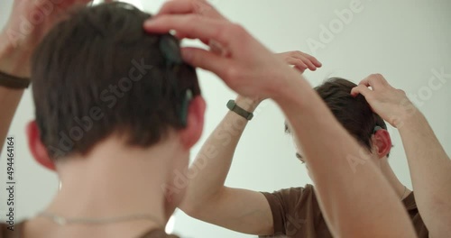 a young man puts on a cochlear implant, a hearing aid, looking at himself in the mirror