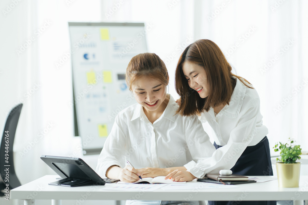 Two Asian businesswoman collegues standing next to each other in an office. They businesswoman talking about report in files.