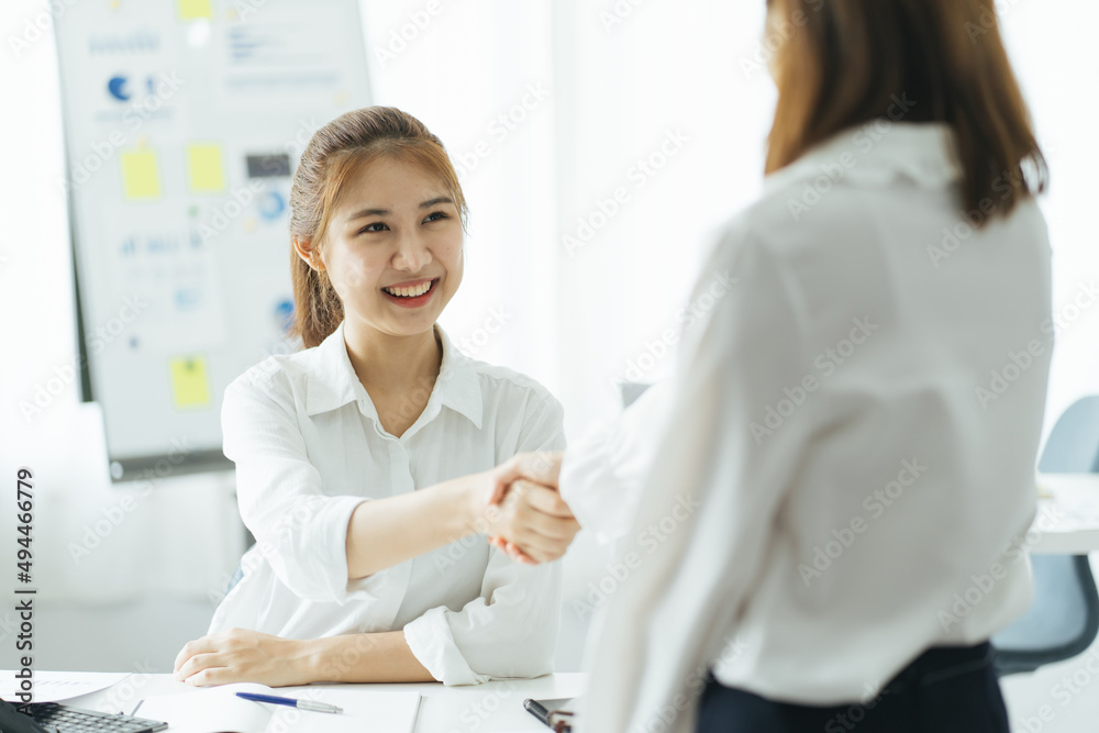 Pretty asian business woman shaking hands with business woman in her office during meeting.