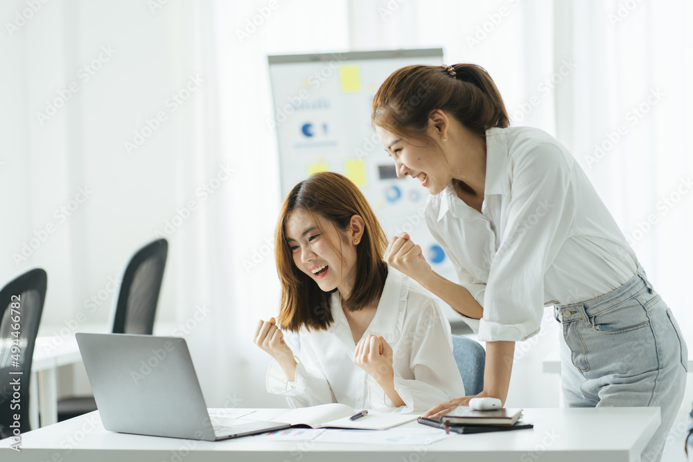 Two pretty young Asian businesswoman sitting at desk with laptop doing paperwork together discussing project financial report. Corporate business collaboration concept. Two pretty young Asian businesswoman sitting at desk with laptop doing paperwork together discussing project financial report. Corporate business collaboration concept.