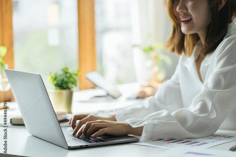 Successful business woman working in a workplace. She feels happy and smiles. Computer laptop and paperwork on desk Successful business woman working in a workplace. She feels happy and smiles. Computer laptop and paperwork on desk