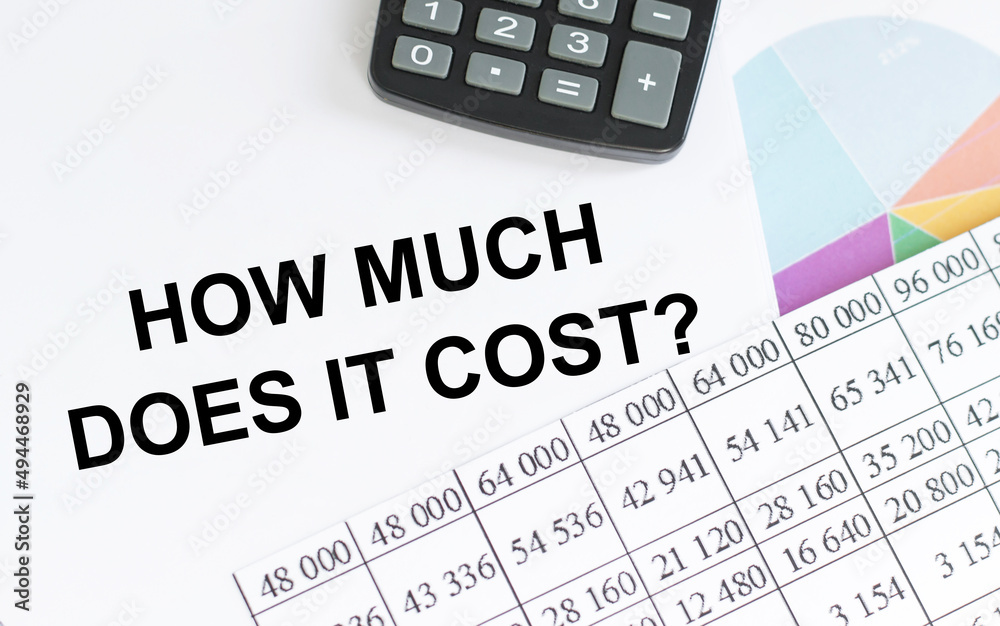 Business concept.Text HOW MUCH DOES IT COST on notepad near calculator, reports, charts Business concept.Text HOW MUCH DOES IT COST on notepad near calculator, reports, charts