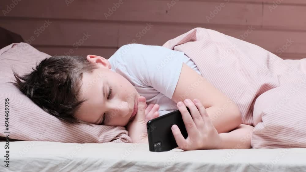 Boy with smartphone is laying in bed, chatting or playing online Boy with smartphone is laying in bed, chatting or playing online