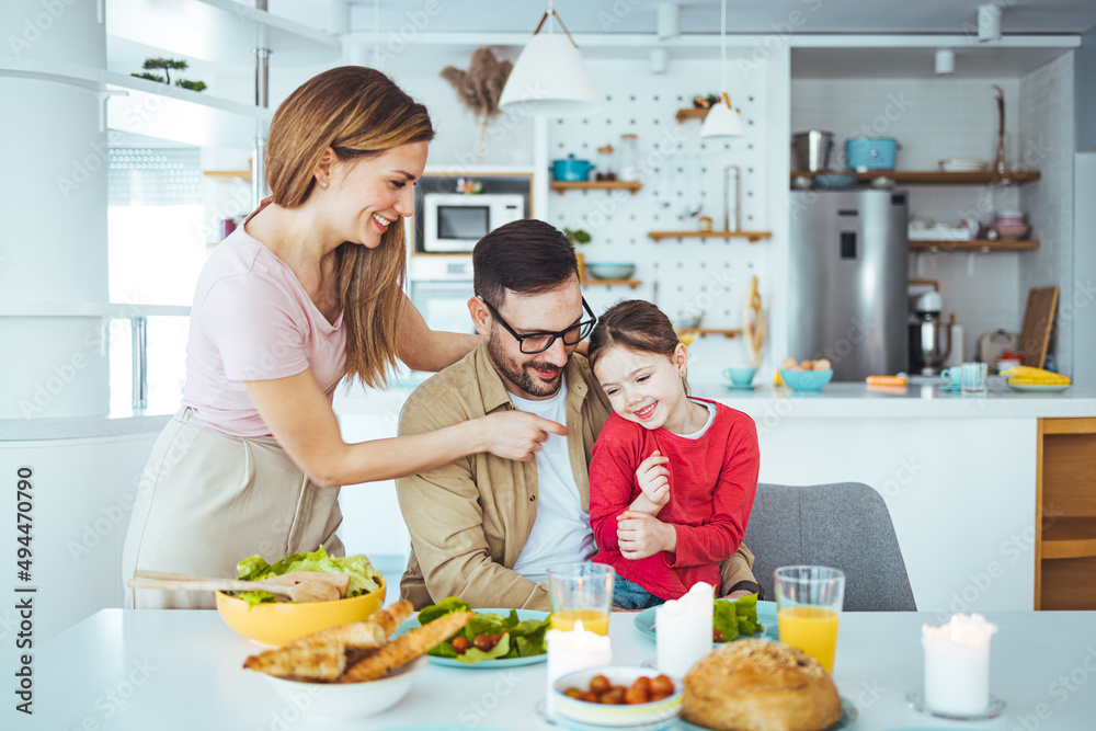 Mom, dad and daughter cook in the kitchen. The concept of a happy family. A handsome man, attractive young women and their sweet daughter eat salad and bread together. Healthy way of living.