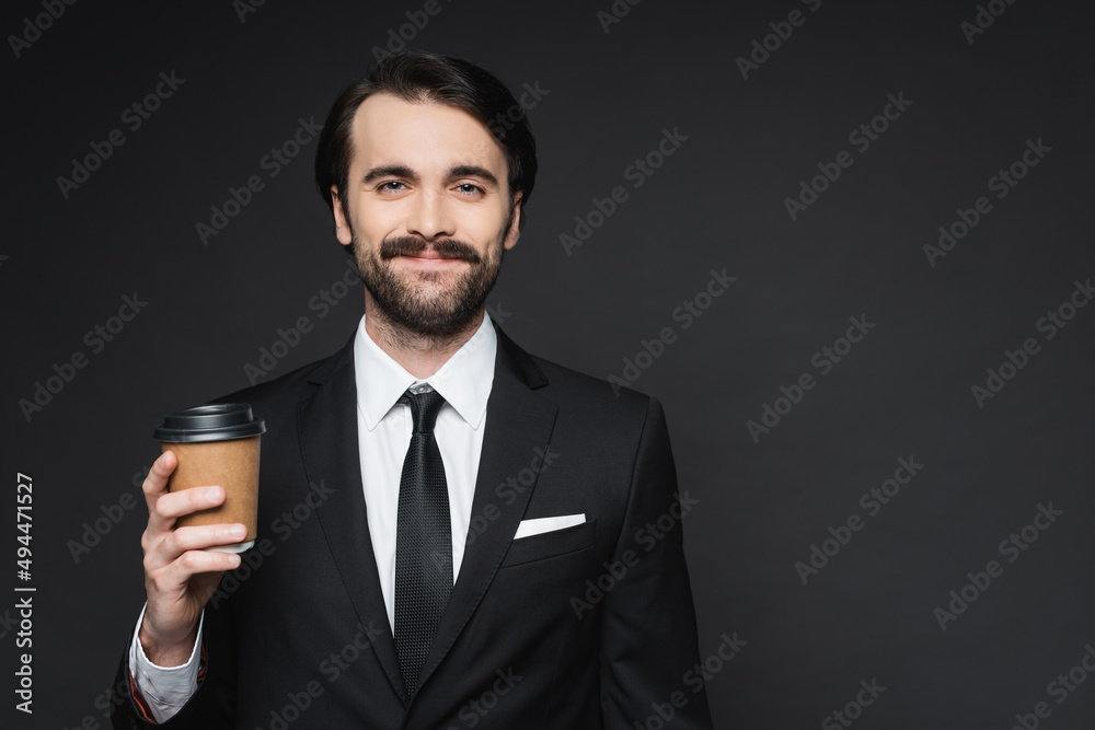 cheerful businessman with mustache holding paper cup on dark grey. cheerful businessman with mustache holding paper cup on dark grey.