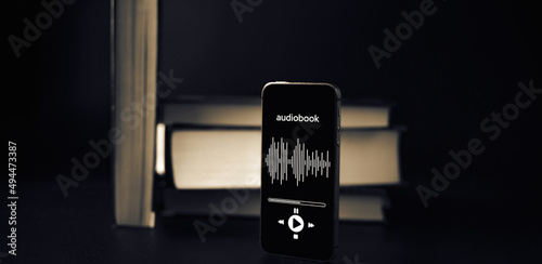 Audio book education. Phone screen with audio book app on paper books black background. Online learning, home school concept.
