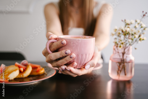 Woman's hand holds a pink mug with coffee, breakfast in a coffee shop