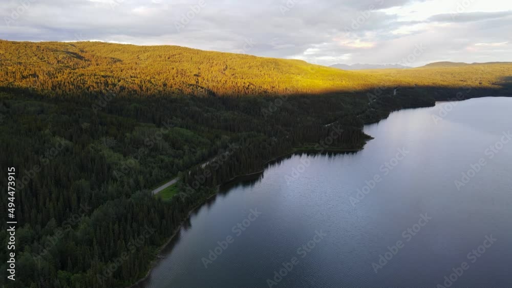 Soft, glowing sunlight hitting the forest treeline surrounding Dease Lake in British Columbia, Canada. Sweeping aerial shot Soft, glowing sunlight hitting the forest treeline surrounding Dease Lake in British Columbia, Canada. Sweeping aerial shot