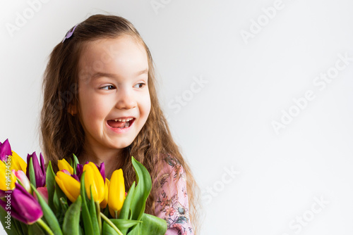 cute girl on a white background with bright flowers tulips. She smiles beautifully.