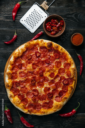 Pepperoni pizza with chili. Round pizza on a dark wooden table