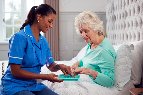 Female Care Worker In Uniform Helping Senior Woman At Home In Bed With Medication photo