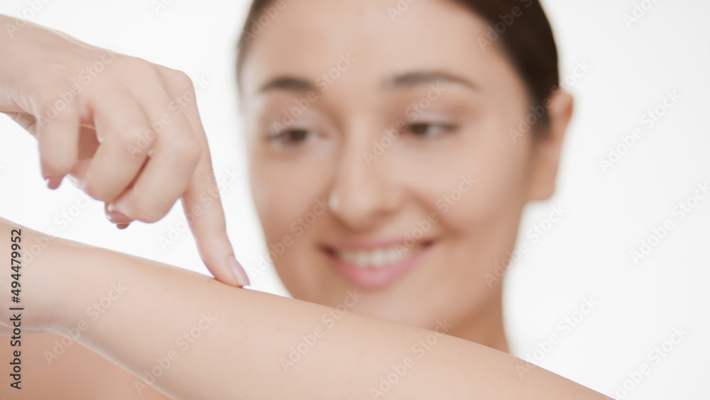 Close-up shot of positive Caucasian woman touches her smooth forearm skin and smiles against white background | After woman shaving concept