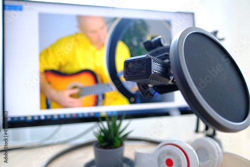 headphones, microphone front of computer, on screen charming elderly man plays guitar, teaches online students online skills, records training video, concept Home Recording Studio