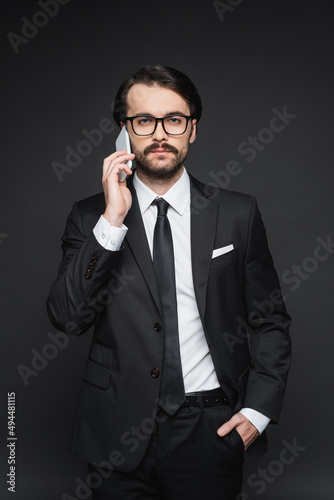 businessman in suit and glasses talking on smartphone on dark grey. © LIGHTFIELD STUDIOS