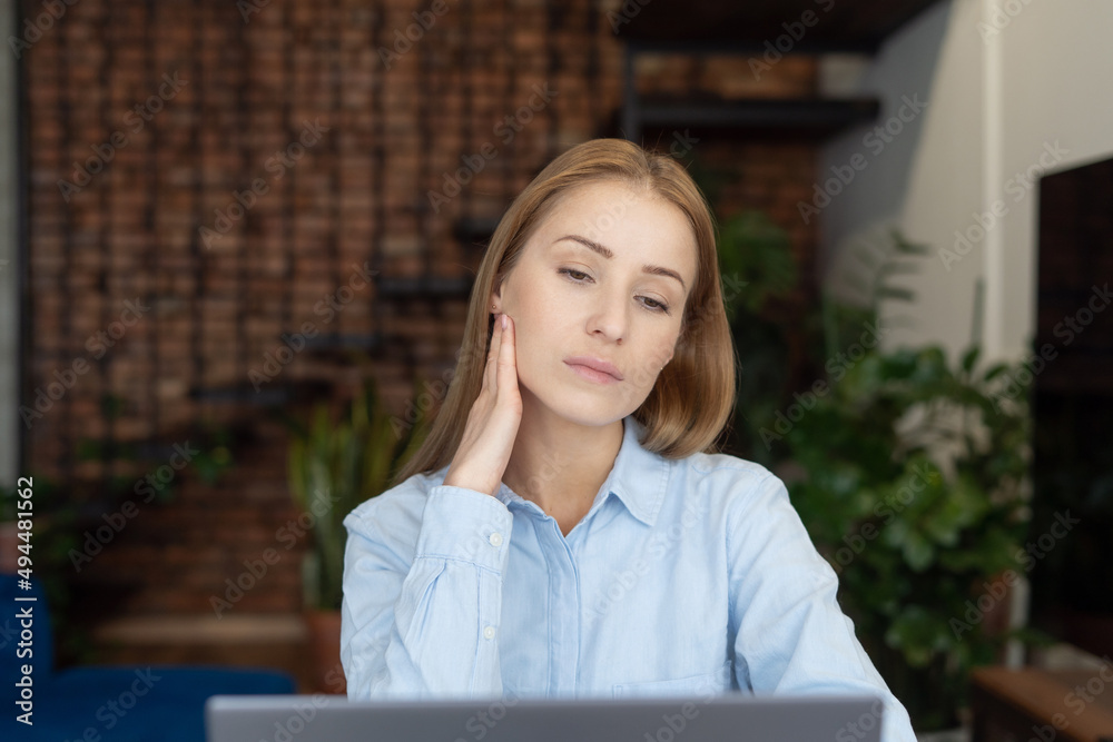 Tired girl looking at laptop while sitting at table Tired girl looking at laptop while sitting at table