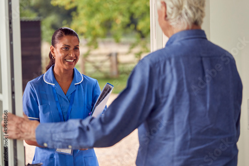 Senior Man Greeting Female Nurse Or Care Worker Making Home Visit In Uniform At Door