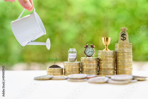 Long-term investment for sustainable growth, financial concept : Hand pours water from a watering can, small tree, saving jar, clock, trophy cup of success / winner prize reward, US dollar bag on coin