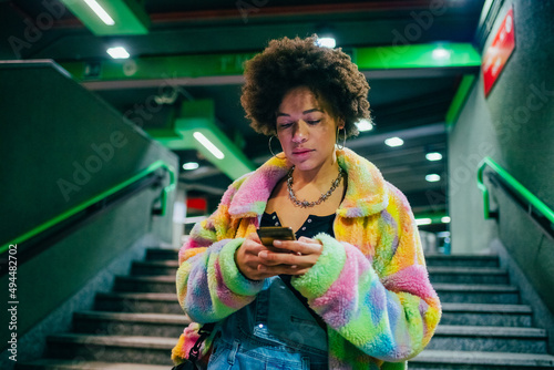 Young mixed race woman indoor metro station using smartphone